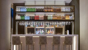 A bar area with multiple shelves of liquor bottles and glasses, and four bar stools. - AC Hotel Som by Marriott (L'Hospitalet de Llobregat)
