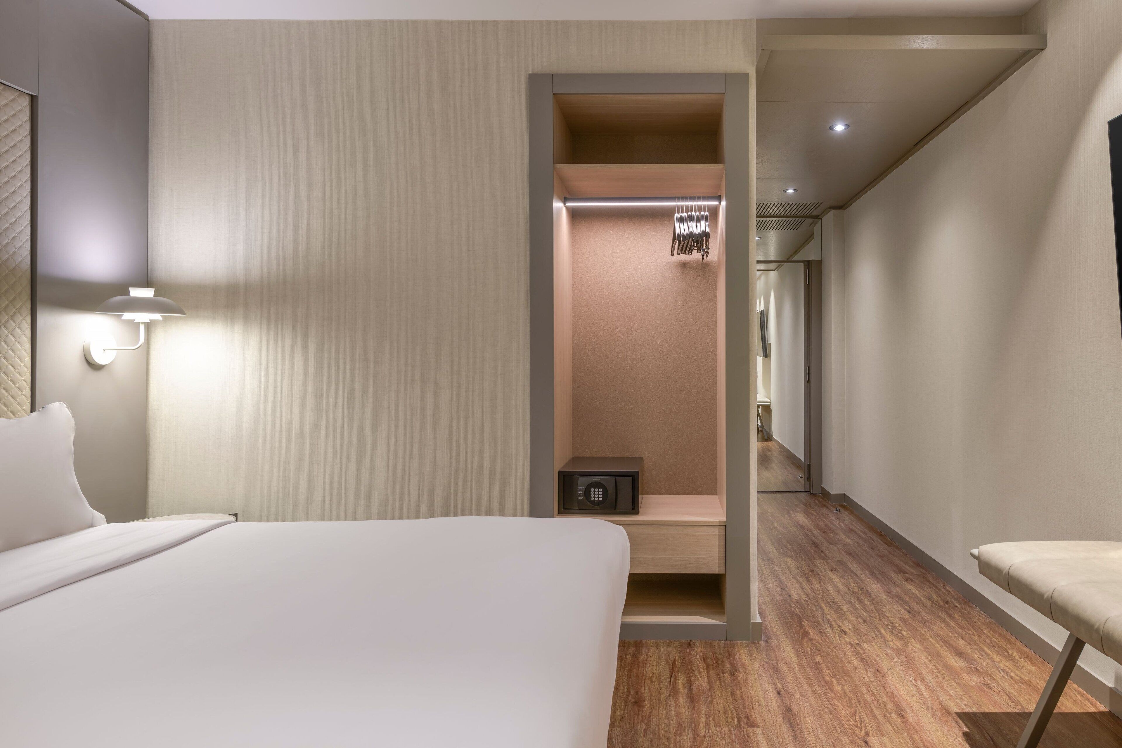 A hotel room with a bed, a nightstand, a lamp, a wardrobe, and a small safe.