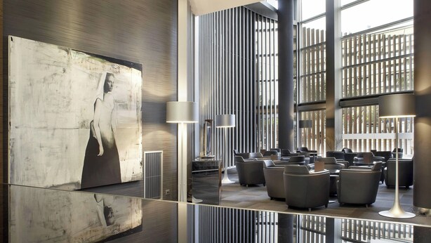 A modern lounge area with a large abstract painting, contemporary furniture, and large windows allowing natural light. - AC Hotel Som by Marriott (L'Hospitalet de Llobregat)