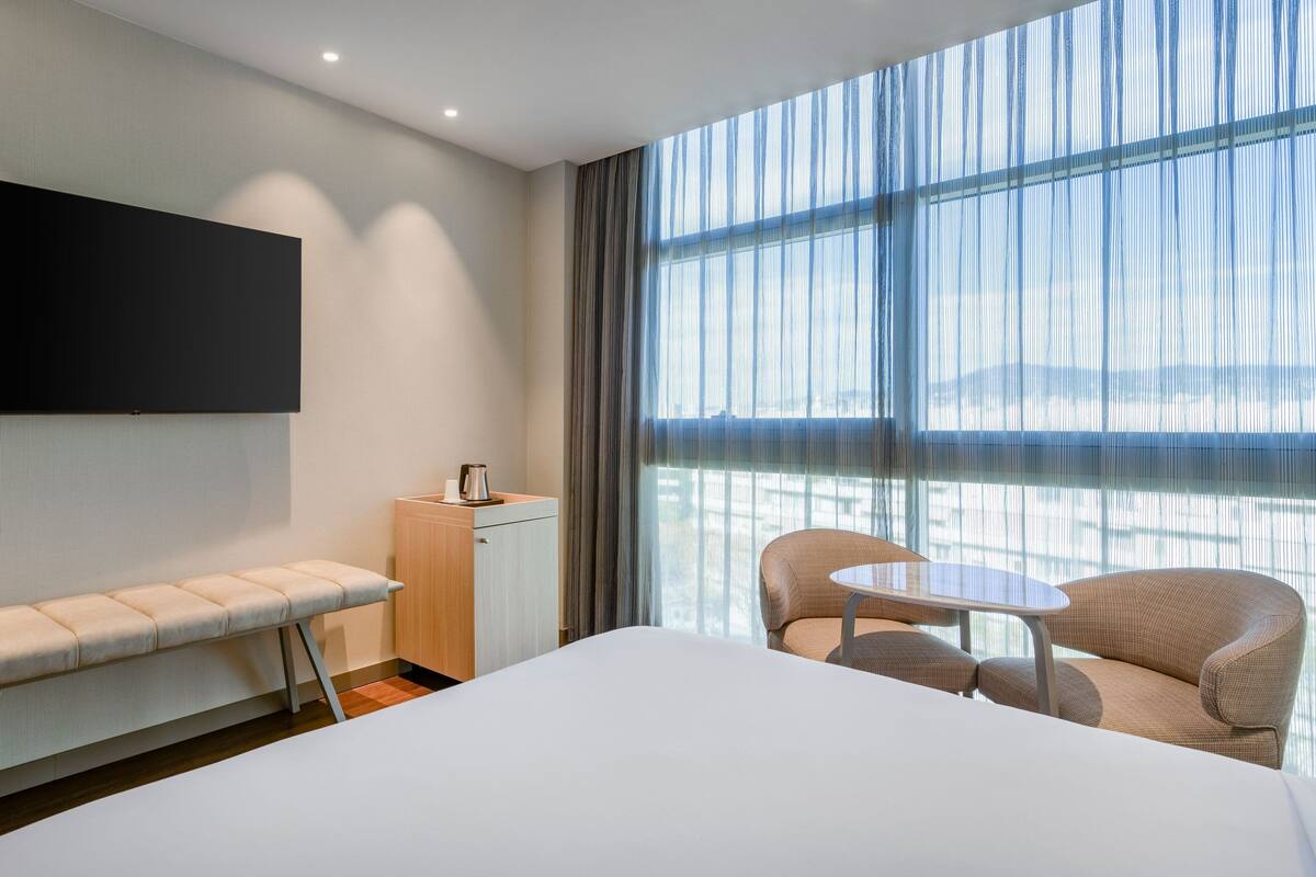 A hotel room with a large bed, a bench, a small table, and a sofa.