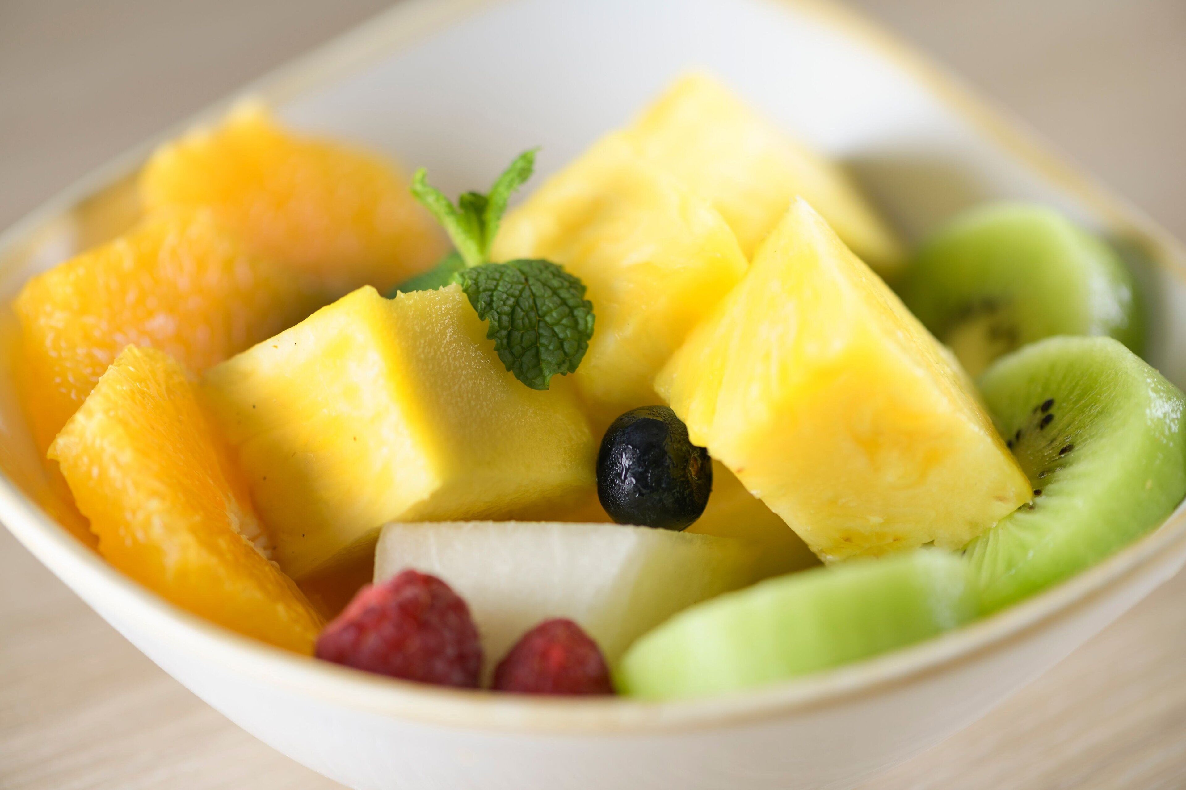 En skål med frukt, inklusive ananas, kiwi, blåbär och hallon.