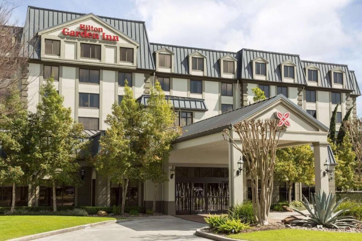 A multi-story hotel with a prominent 'Hilton Garden Inn' sign, a covered entrance, and a landscaped front yard.