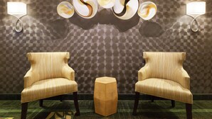 Une pièce comprenant deux fauteuils, une table hexagonale et des lampes fixées au mur, le tout sur un mur à texture.