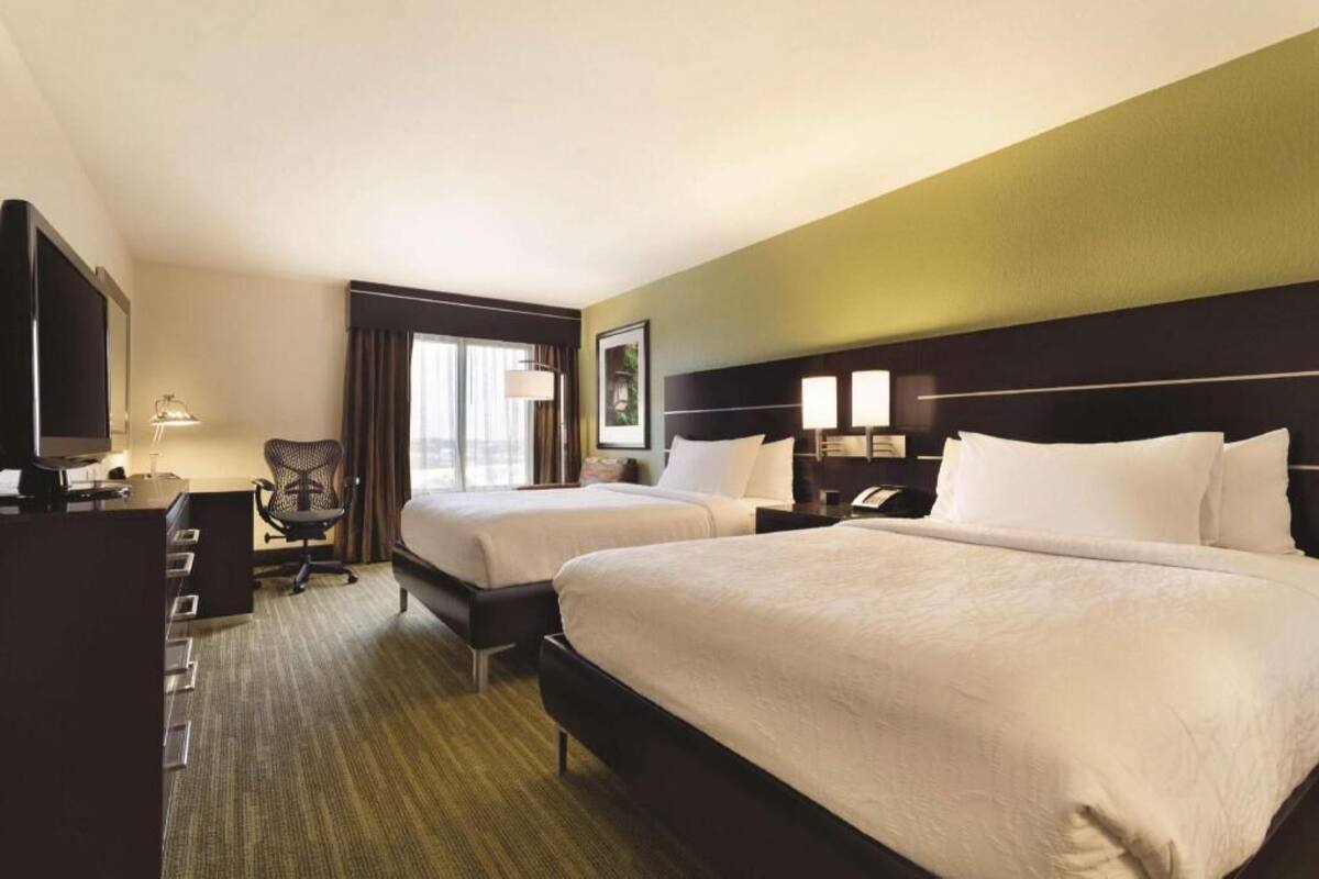 A hotel room with two beds, a desk, a chair, and a television.