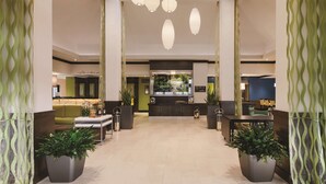 Un hall d’entrée spacieux avec un plafond haut, de nombreuses suspensions décoratives et de grandes plantes en pot.