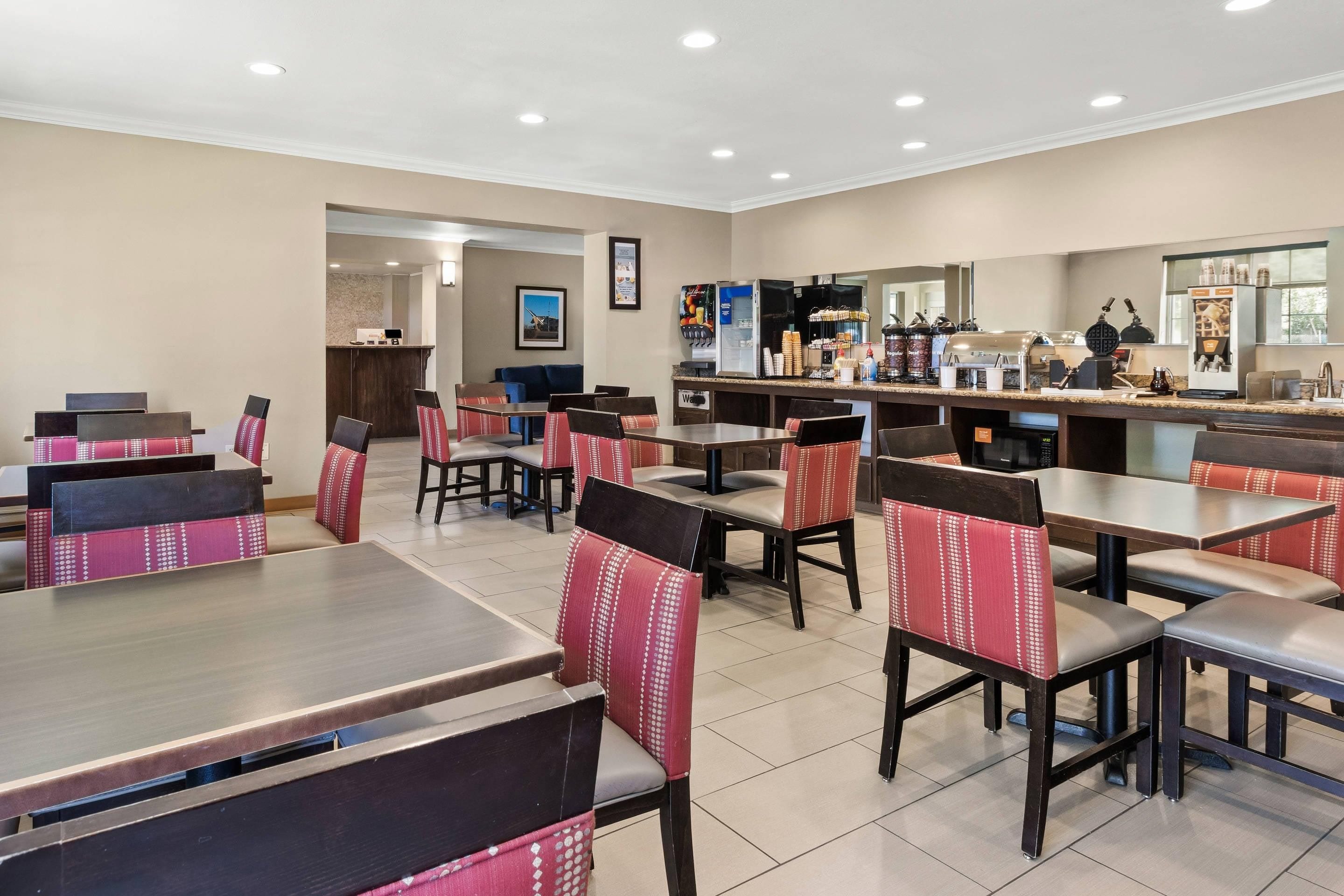 A restaurant with multiple tables and chairs, a counter with a coffee machine, and a kitchen area in the background.