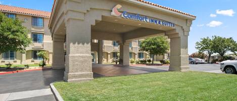 A Comfort Inn & Suites building with a covered entrance, a parking lot, and a well-maintained lawn.