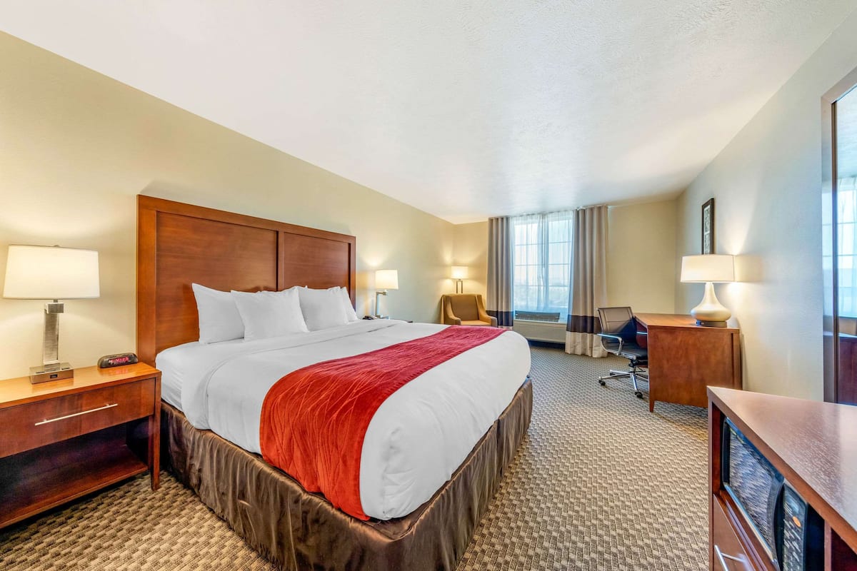 A hotel room with a large bed, a desk, a chair, and a window with curtains.