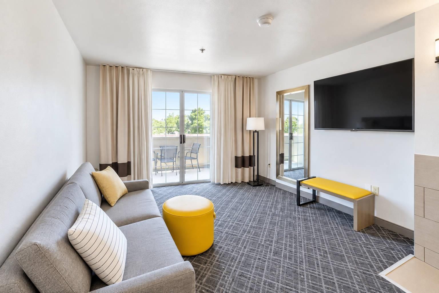 Une chambre d’hôtel équipée d’un canapé, d’un pouf, d’un banc et d’un téléviseur à écran plat.