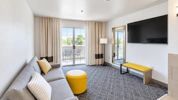 Une chambre d’hôtel équipée d’un canapé, d’un pouf, d’un banc et d’un téléviseur à écran plat.