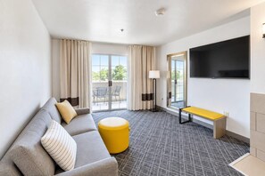 Une chambre d’hôtel équipée d’un canapé, d’un pouf, d’un banc et d’un téléviseur à écran plat.