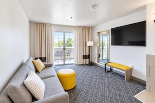 Una habitación de hotel con sofá, reposapiés, banco y televisor de pantalla plana.