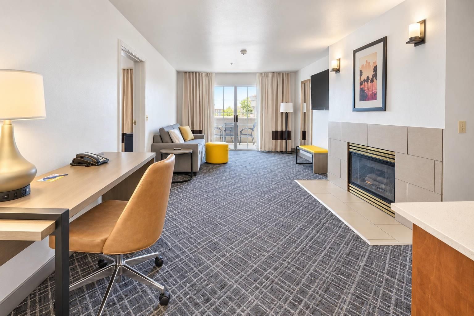 A hotel room with a desk, chair, sofa, and a fireplace.