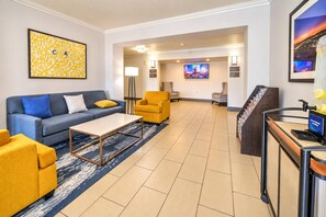 A hotel lobby with a blue sofa, yellow armchairs, a coffee table, a reception desk, and a TV screen. - Comfort Inn & Suites Lancaster Antelope Valley (Lancaster)