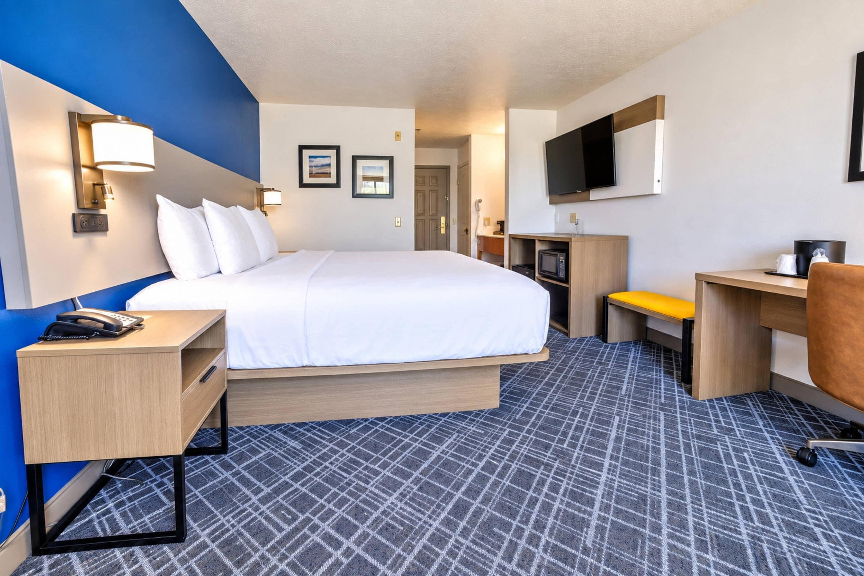 A hotel room with a bed, desk, chair, and a TV.