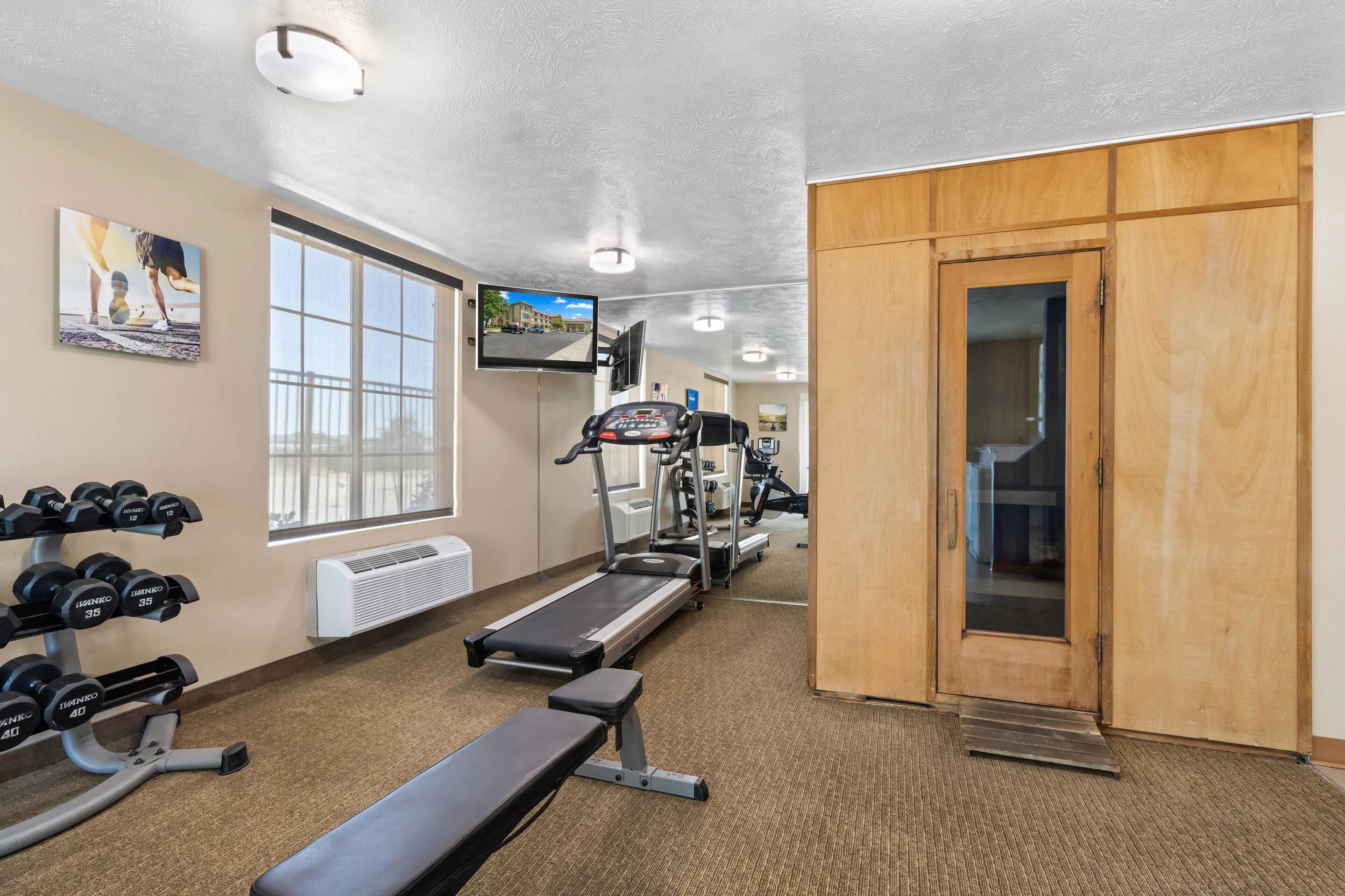 Une salle de sport équipée de matériel d’exercice, d’un banc et d’un téléviseur fixé au mur.