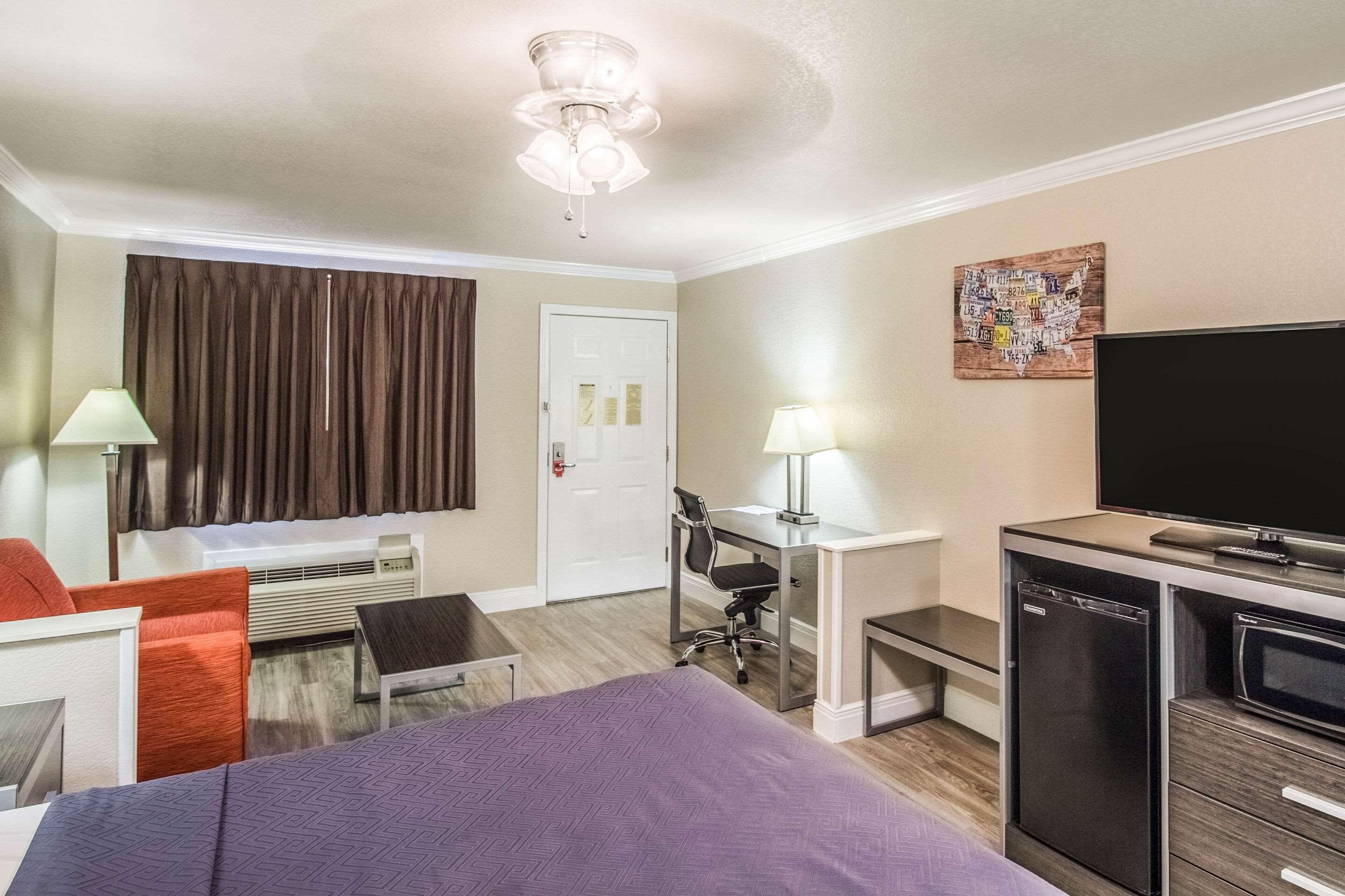 Una habitación de hotel con cama, escritorio, silla, televisor y refrigerador.
