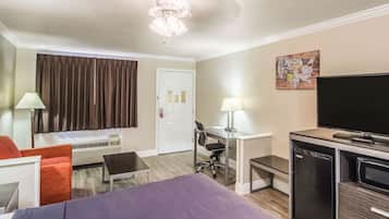A hotel room with a bed, desk, chair, television, and a refrigerator.