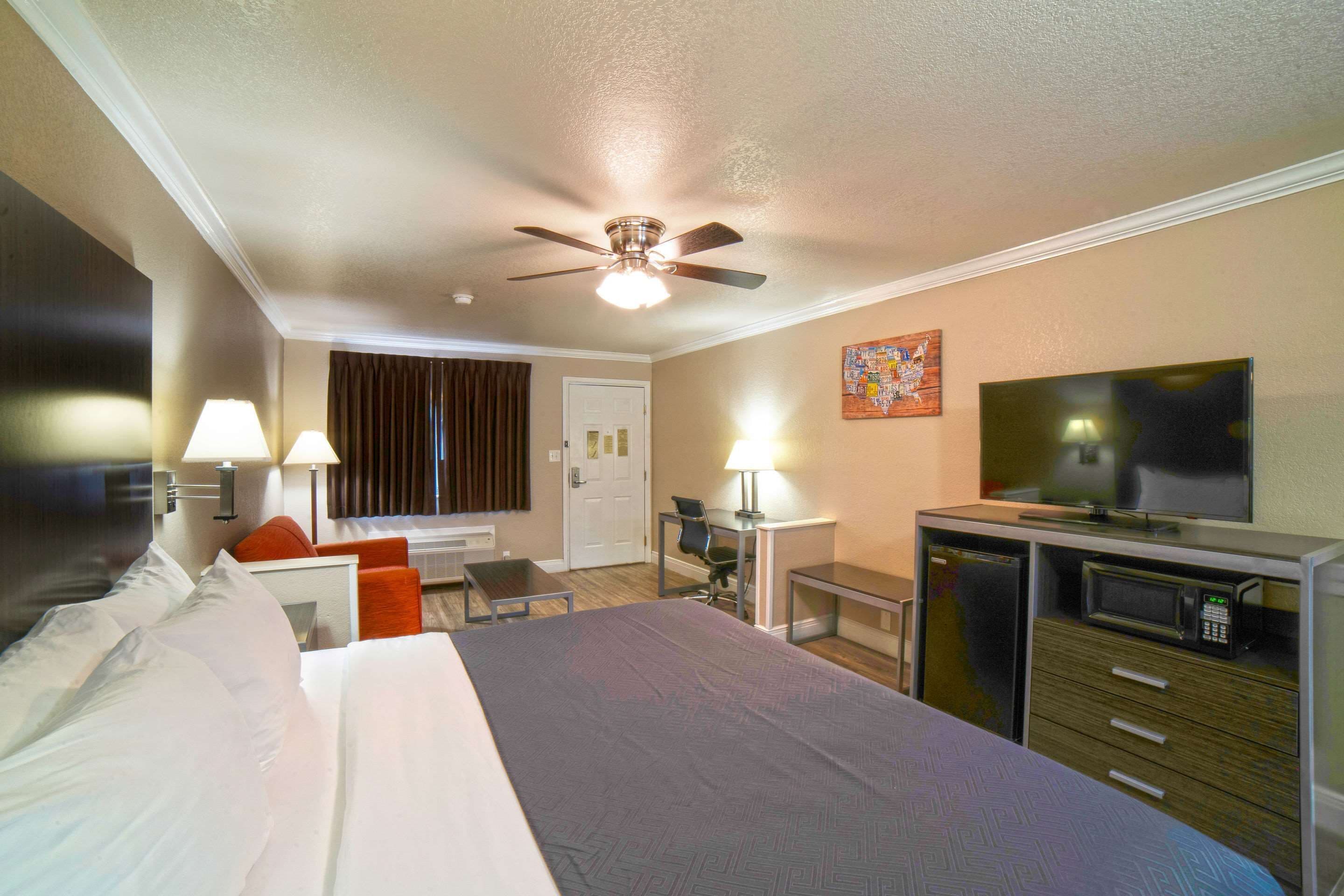 Habitación de hotel con cama, escritorio, silla, televisor, microondas y ventilador de techo.