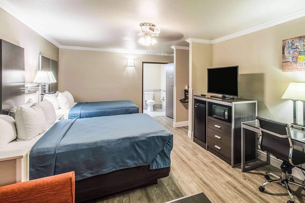 A hotel room with two beds, a desk with a TV, a microwave, and a chair.