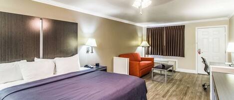 Een hotelkamer met een groot bed, een bureau, een stoel, een bureaulamp, een plafondventilator en een raam met gordijnen.