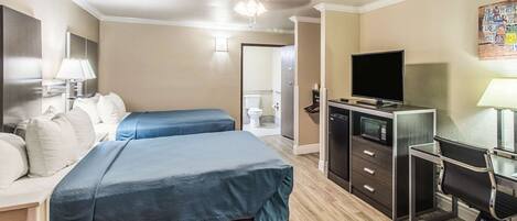 A hotel room with two beds, a desk with a computer, a TV, and a bathroom visible through an open door.