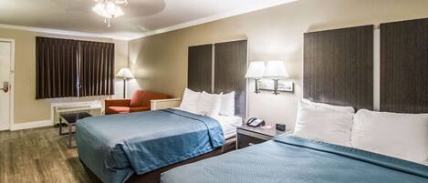 A hotel room with two beds, a desk, a chair, a lamp, and a ceiling fan.
