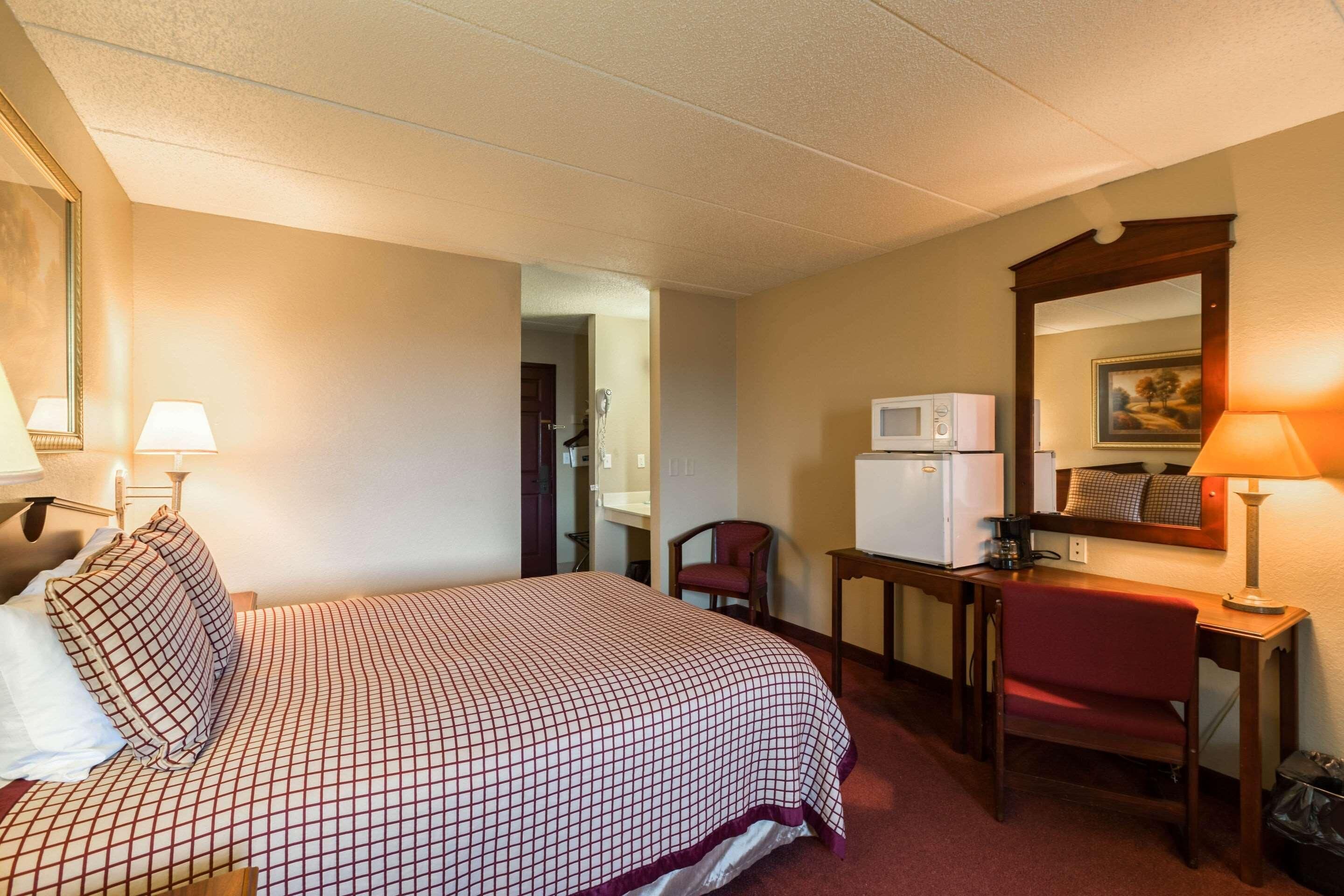 A hotel room with a bed, a desk, a chair, a microwave, and a television.
