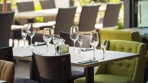A restaurant with tables set for dining, chairs, and a green upholstered chair. - Hotel Am Wald (Monheim)