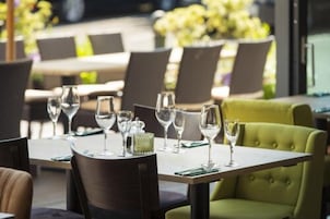 Um restaurante com mesas postas para refeições, cadeiras e uma poltrona estofada verde.