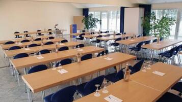 Un salón de conferencias con varias mesas y sillas, una pantalla de proyector y ventanas amplias.