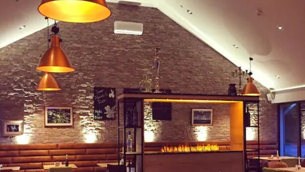 A restaurant with wooden booths, tables, and hanging pendant lights. - Hotel Am Wald (Monheim)