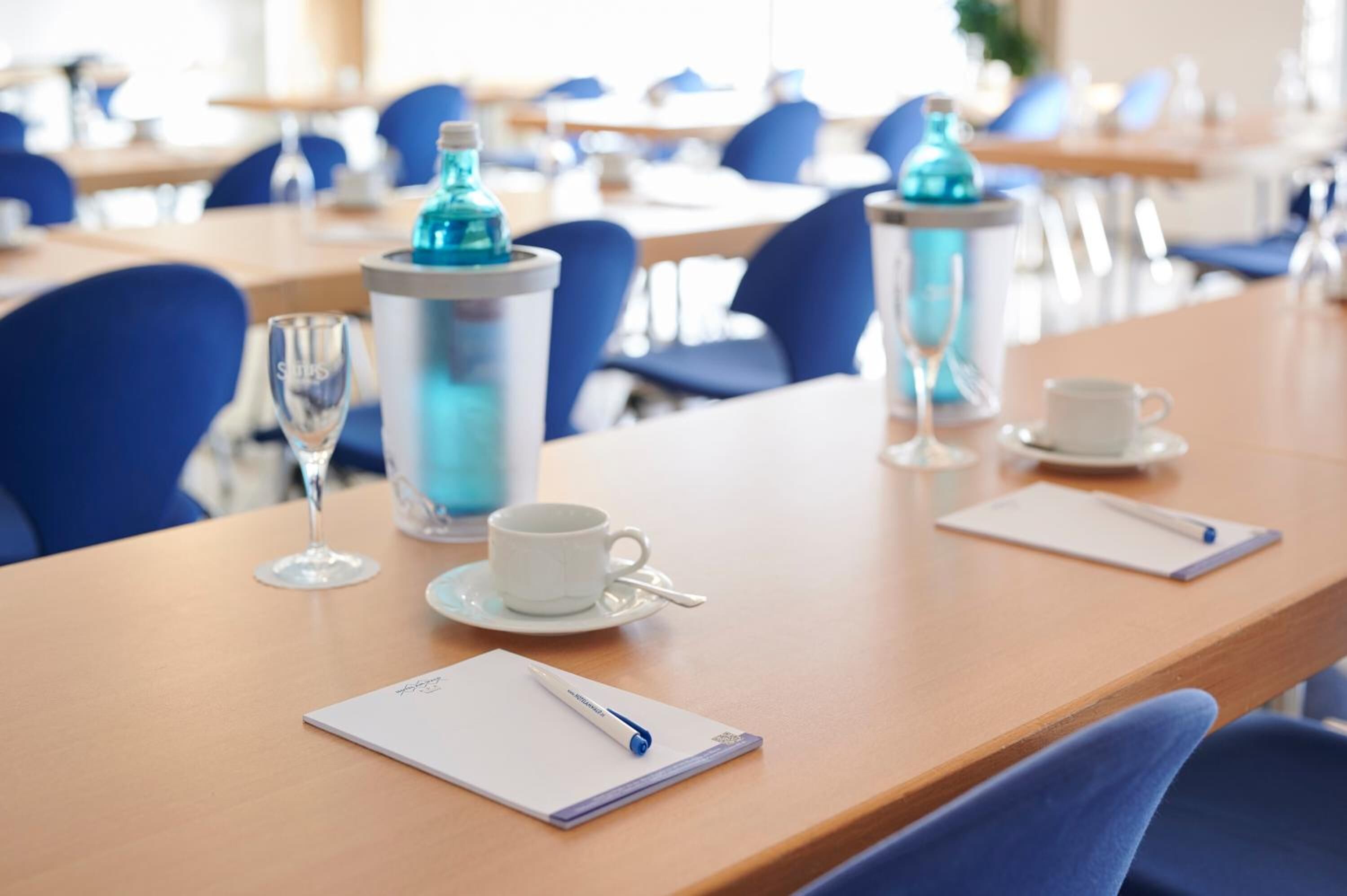 A conference room with a wooden table, a white cup, a glass, a pen, and a notebook.