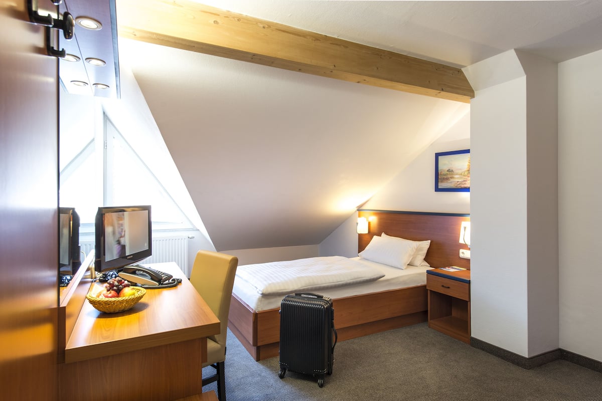 Quarto de hotel com cama, escrivaninha, cadeira e mala.