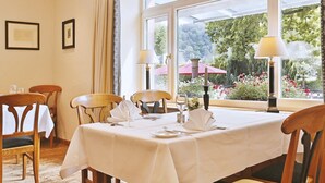 Un comedor con una mesa preparada para cuatro, sillas y vistas a un jardín a través de amplios ventanales.