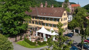 Un hotel con fachada amarilla, múltiples ventanas y un patio con mesas al aire libre.