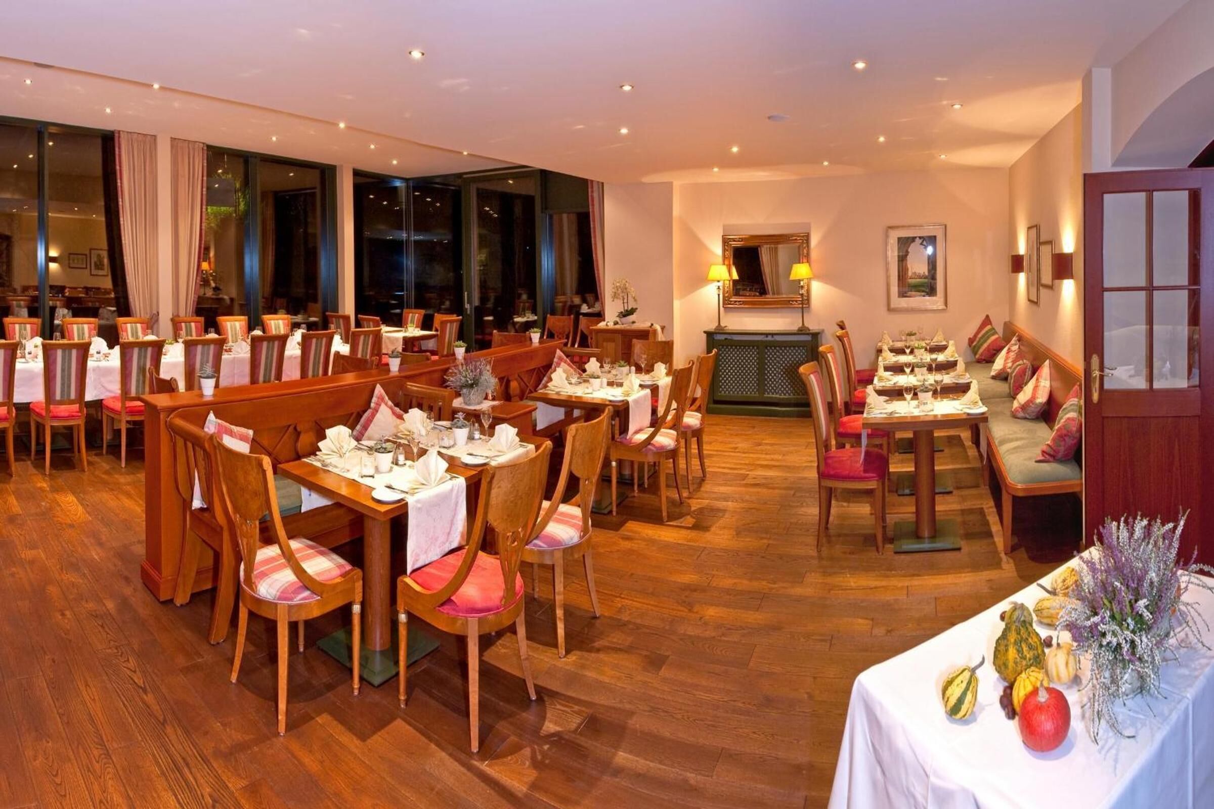 Un restaurante con varias mesas y sillas, suelo de madera y amplios ventanales.