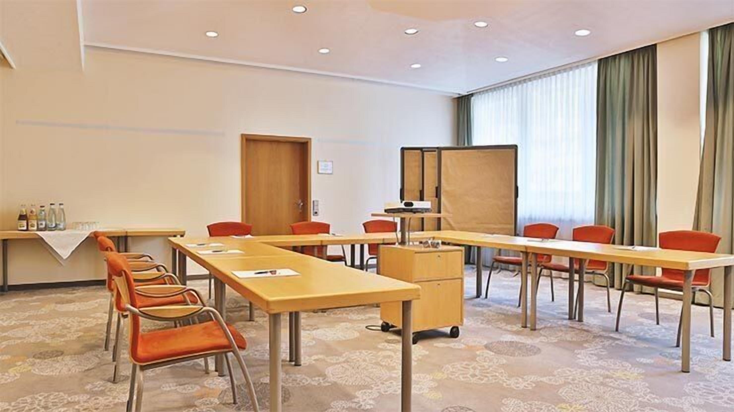 Una sala de conferencias con mesas largas, sillas, una pizarra y un proyector.