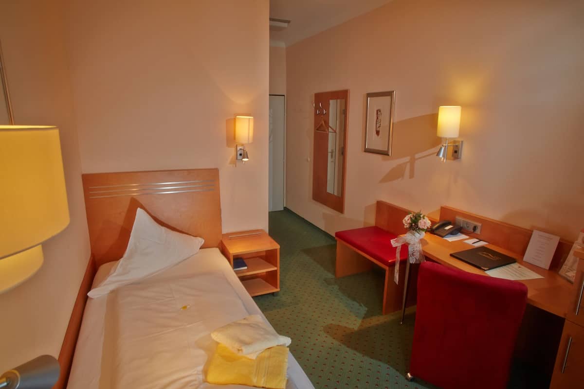 A hotel room with a bed, bedside table, a desk with a chair, and a small seating area.
