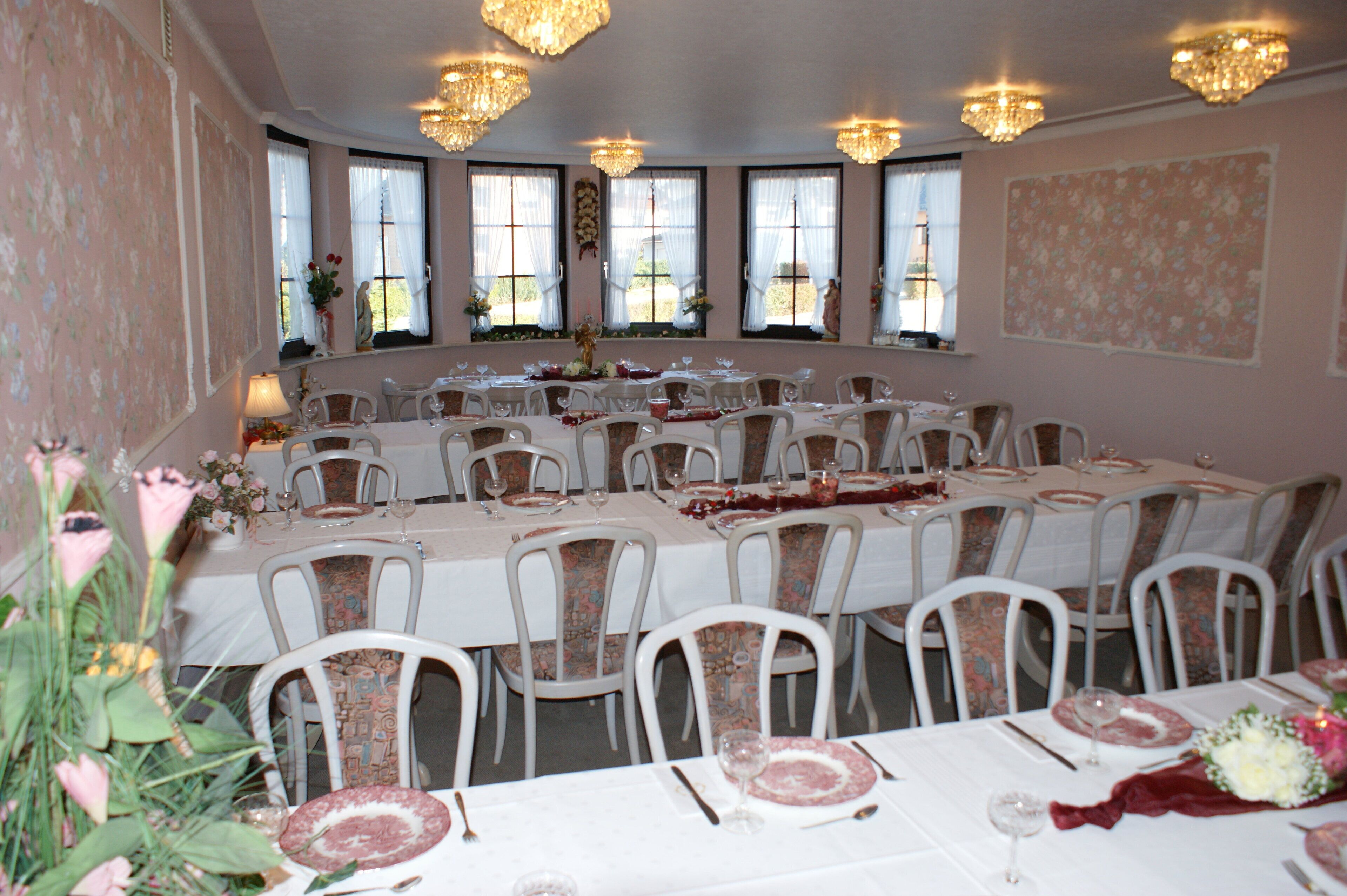 A banquet hall with round tables set for dining, white chairs, and chandeliers.