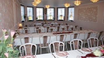 A banquet hall with round tables set for dining, white chairs, and chandeliers.