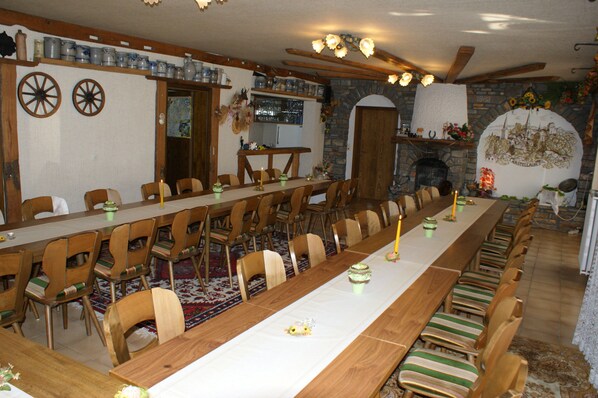 Una larga mesa de comedor con sillas, una zona de cocina con pared de piedra y una chimenea con un mural.