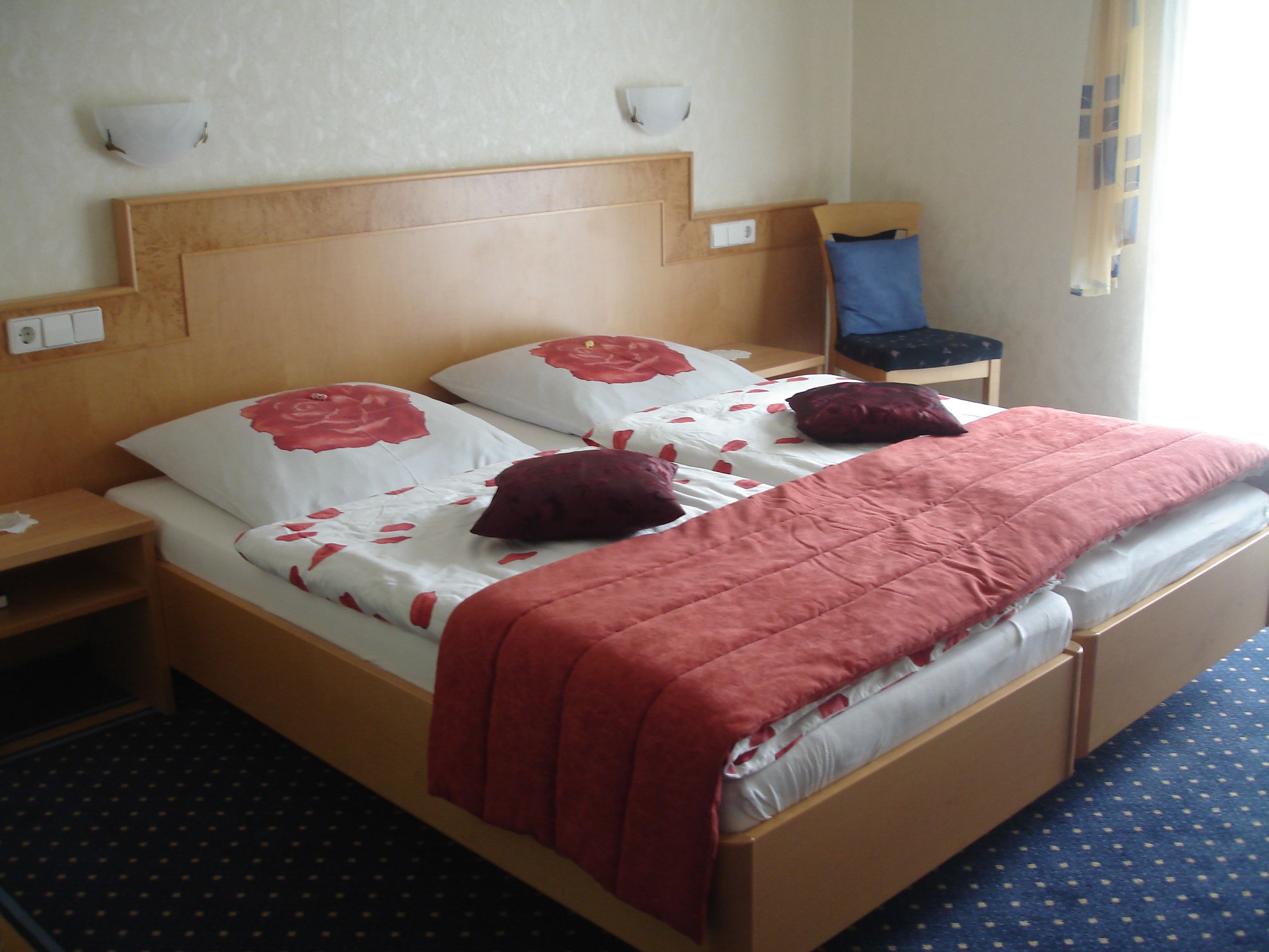 Ein Doppelbett mit Holz-Kopfstück, zwei Nachttische und ein blauer Teppich mit Muster.