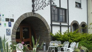 A courtyard with a stone bench, potted plants, and white metal chairs. - Hotel Zum Rehberg (Kastellaun)