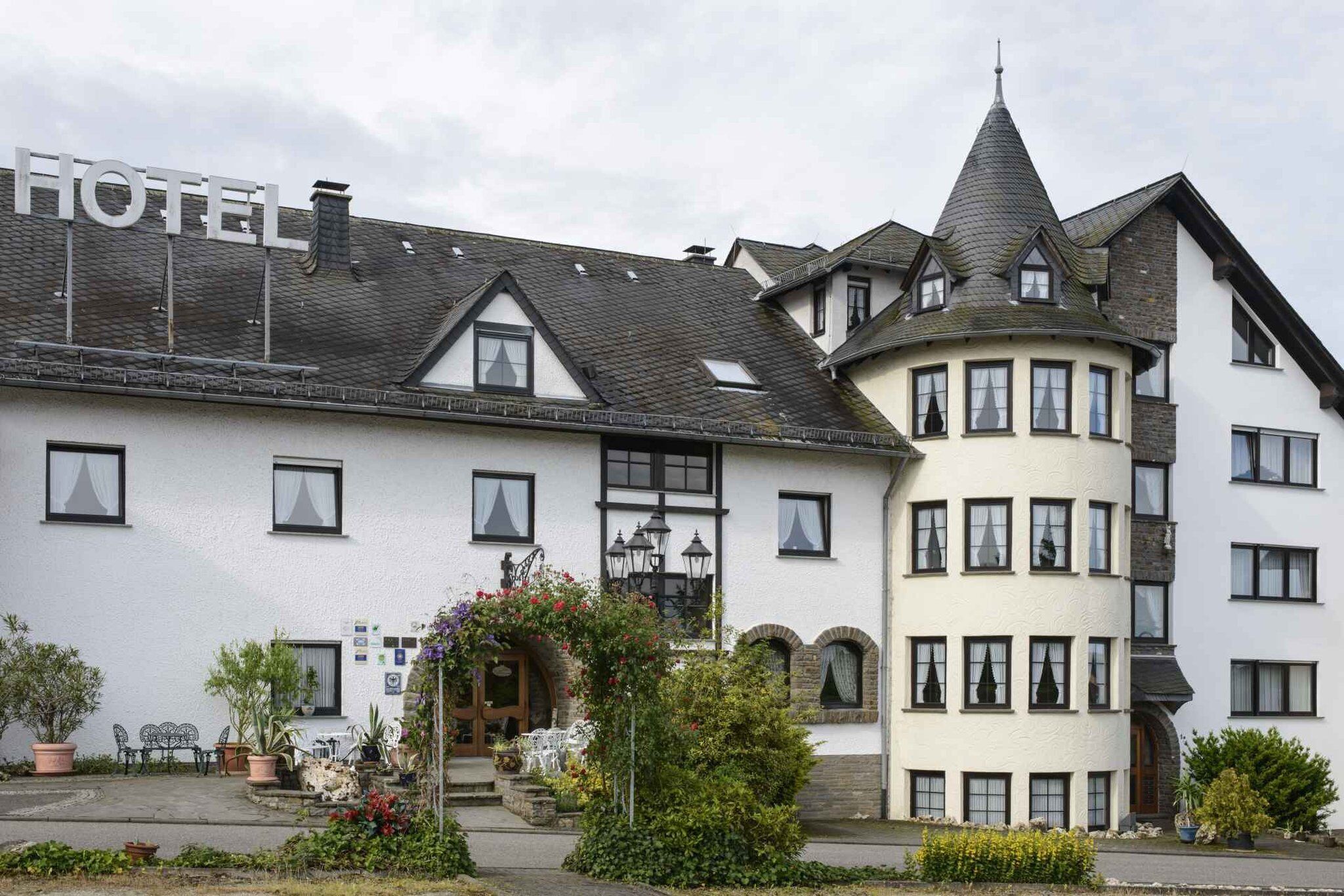 Ein Hotel mit einem gut sichtbaren 'HOTEL'-Schild, traditioneller Architektur inklusive eines Turms und einem gepflegten Garten.