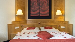 A hotel room with a wooden headboard, two bedside lamps, a bed with rose-patterned pillows, and a large framed artwork above the bed. - Hotel Zum Rehberg (Kastellaun)