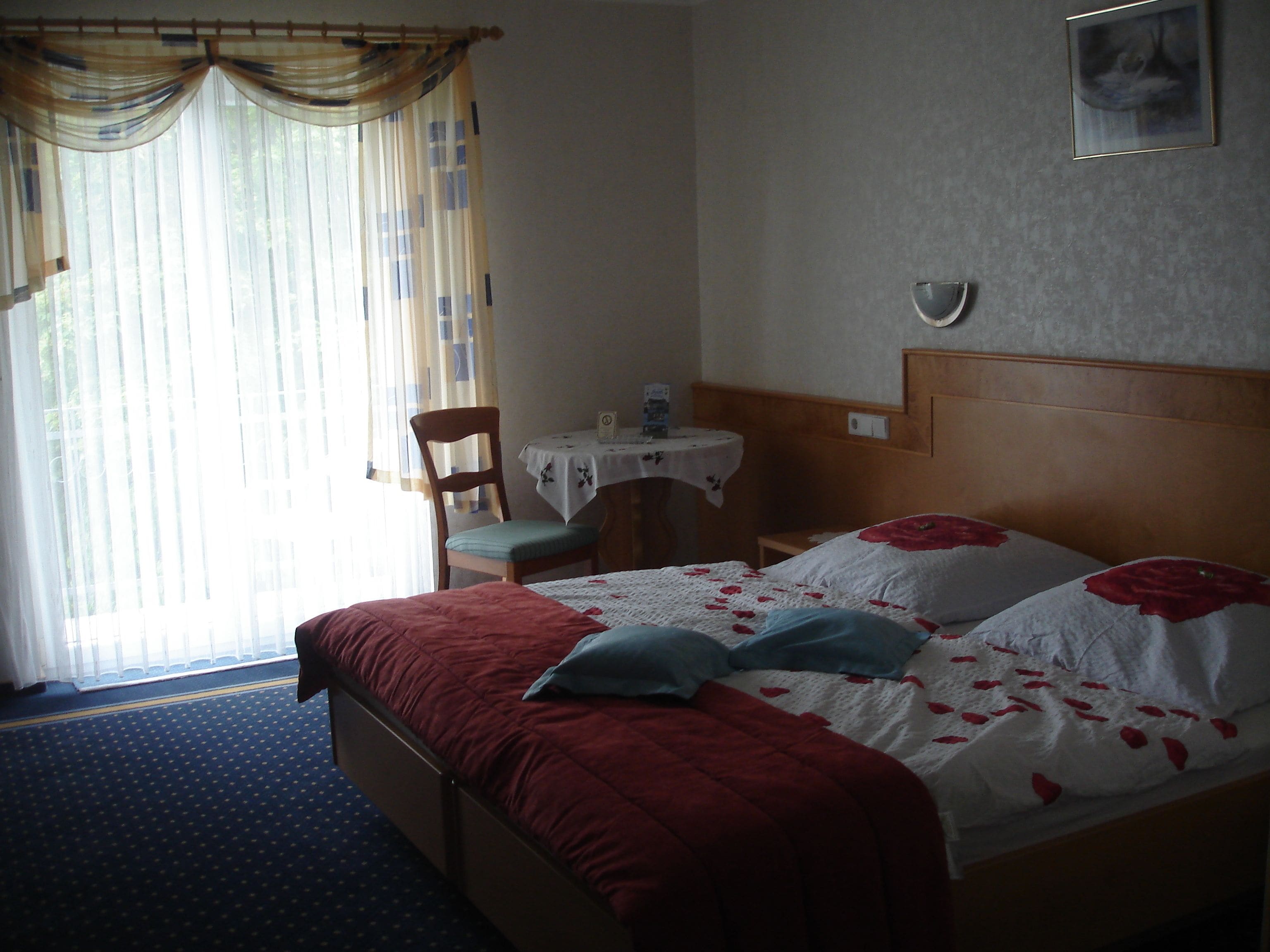 A hotel room with a bed, a chair, a small table, and a window with curtains.