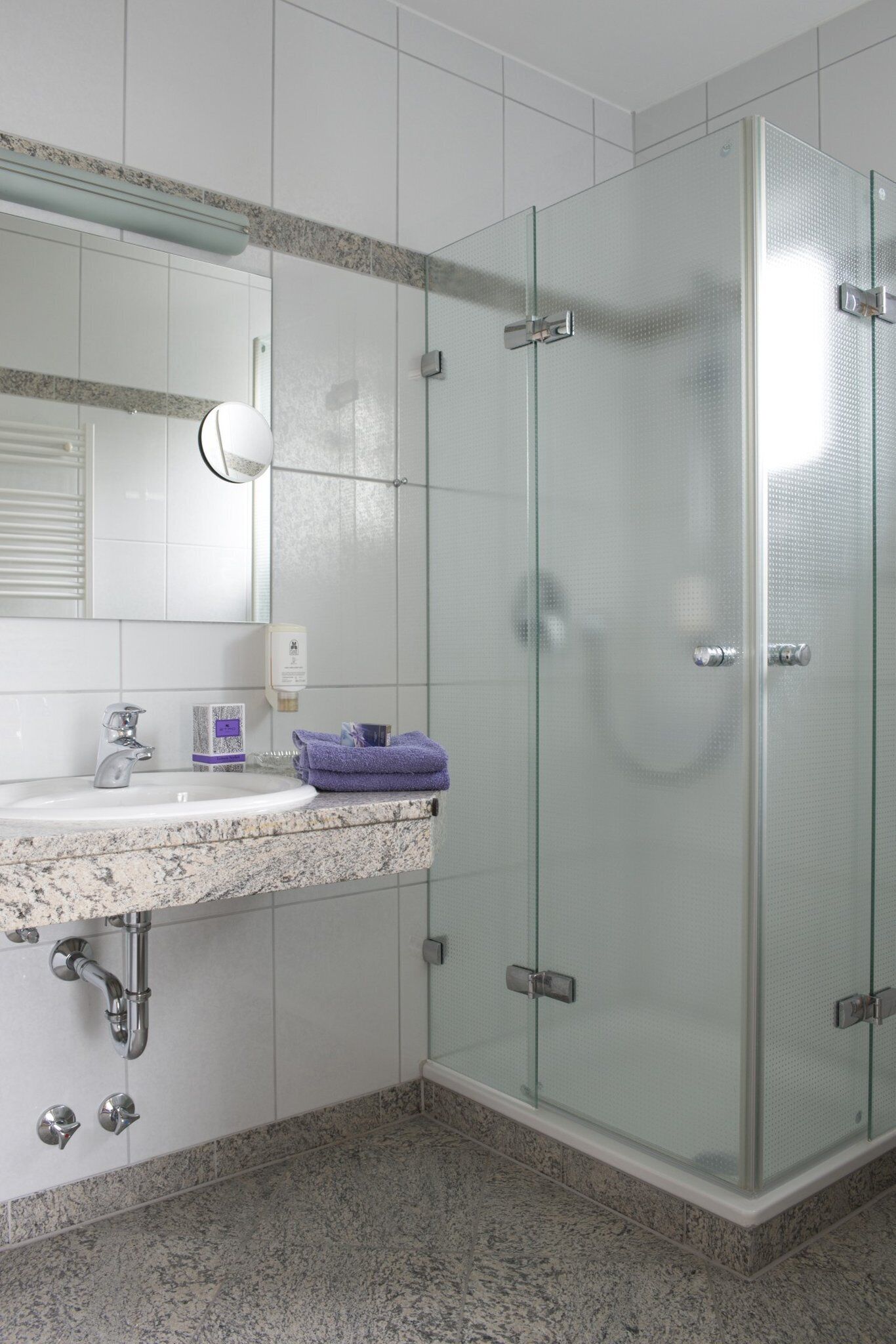 A bathroom with a glass shower enclosure, a sink with a marble countertop, and a mirror above the sink.