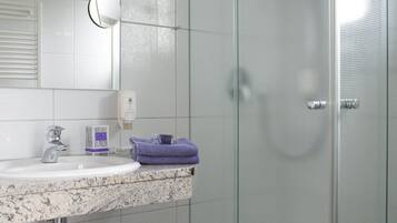 A bathroom with a glass shower enclosure, a sink with a marble countertop, and a mirror above the sink.