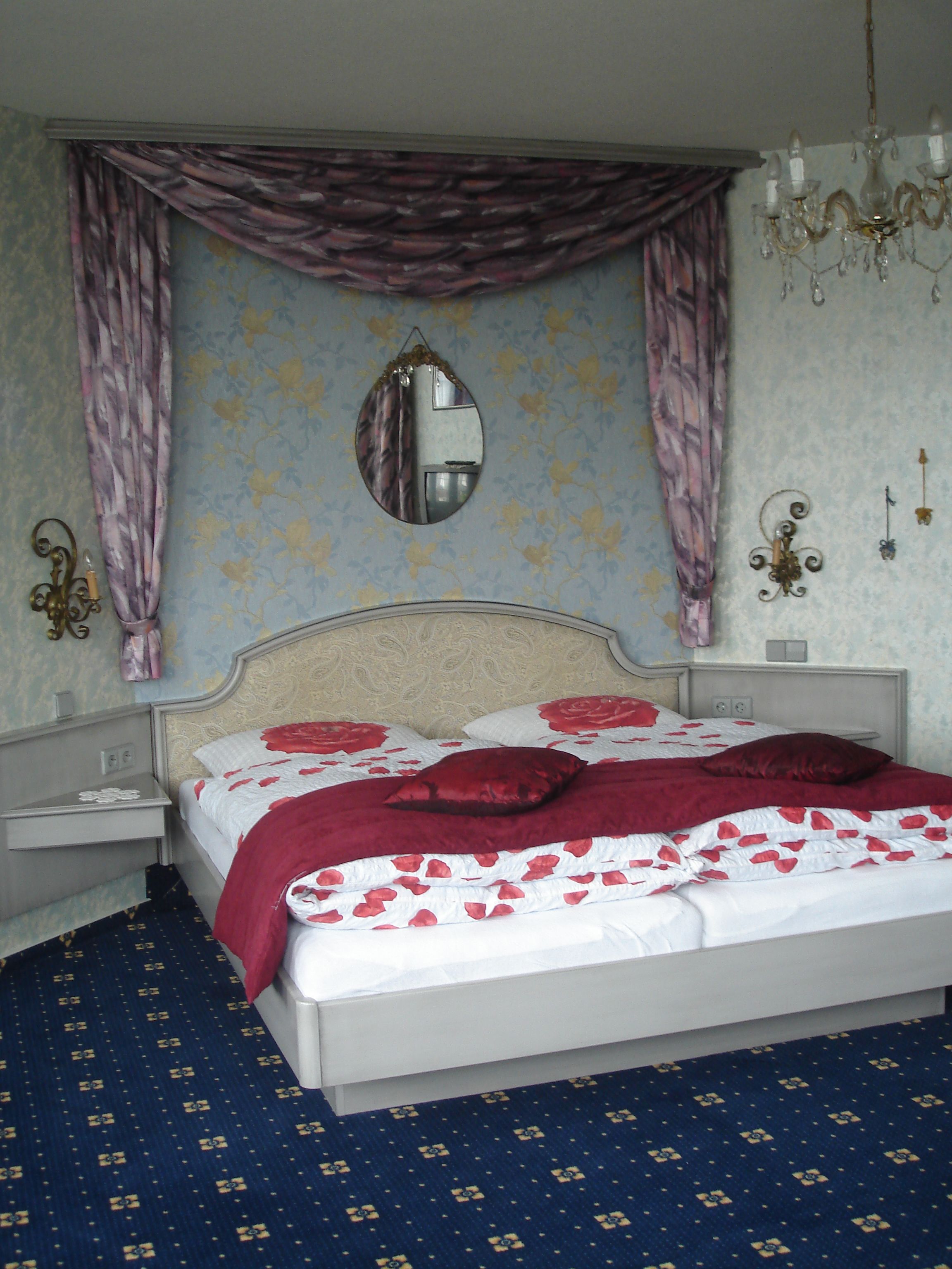 Un lit bien fait, recouvert d’une couvre-lit à motifs floraux, avec un miroir au-dessus et un lustre suspendu au plafond.